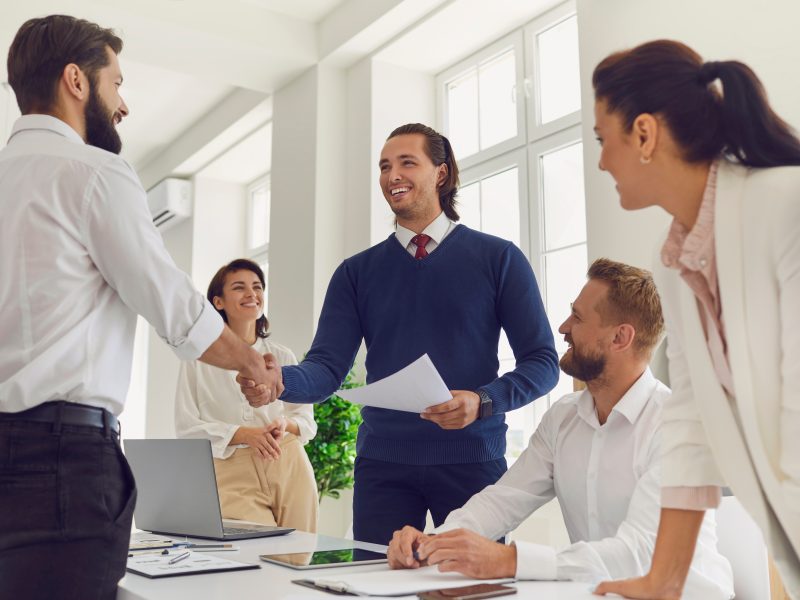 Friendly business team manager shaking hands with happy employee during work meeting